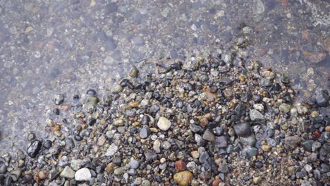 Close-up-of-crystal-clear-water-lapping-over-colorful-pebbles