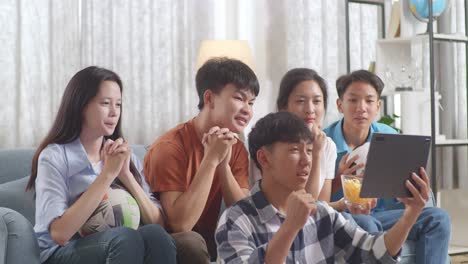 asian teenagers cheering and watching football game on tablet and celebrating victory at home