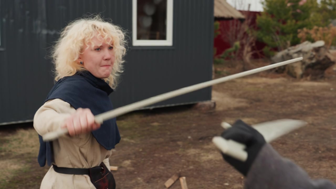 Barn i mantlar sparras med träsvärd på en rustik bakgård, där en kliver tillbaka medan den andra svingar, vilket skapar livlig utomhusrörelse, vänlig interaktion och fantasifull lek i dagsljus.