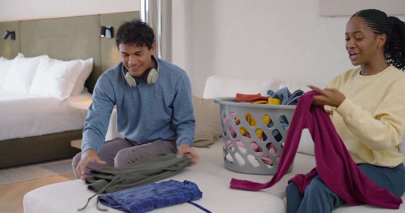 African American couple folding clothes on sofa from laundry basket after woman handing plaid shirt