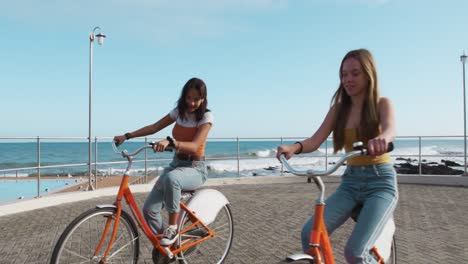 side view of a caucasian and a mixed race girl riding a bike seaside