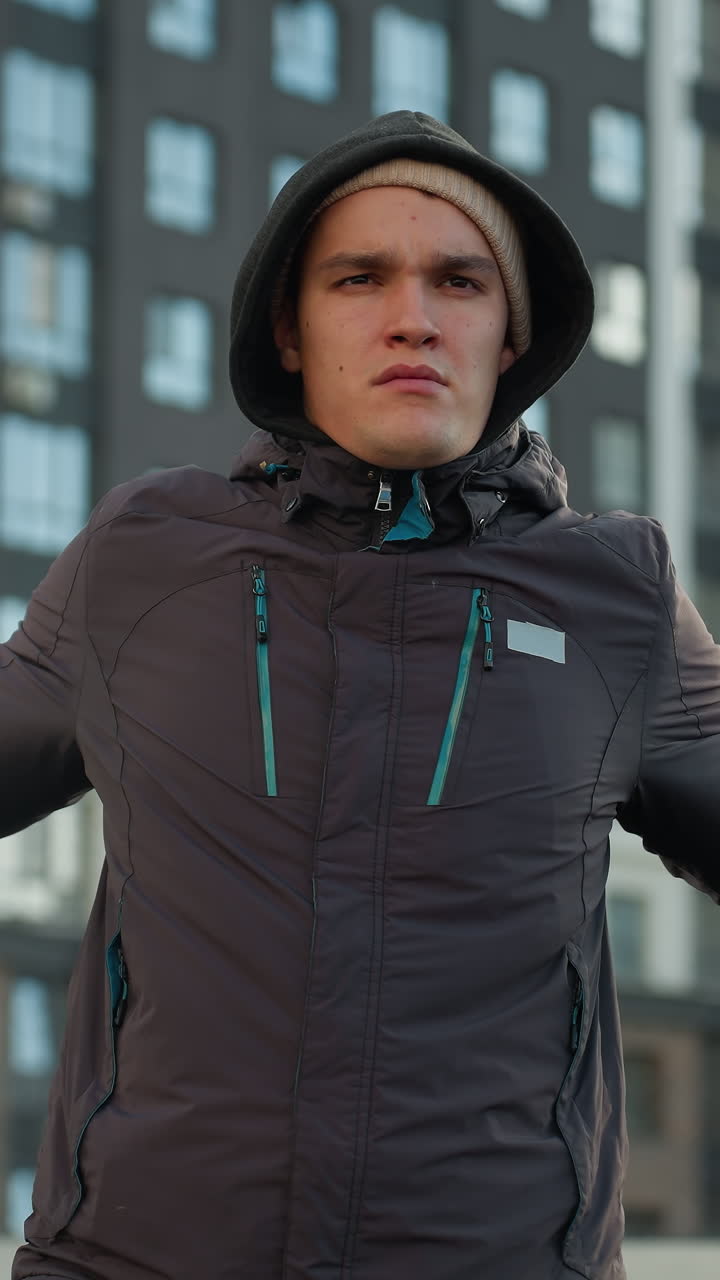 Athlete preparing for sport activity, turning head and stretching arms while wearing hoodie in urban sports arena surrounded by residential buildings