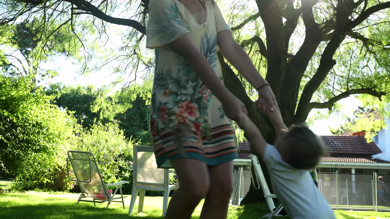 madre girando en círculos con el bebé bebé hijo afuera en el patio trasero de la casa