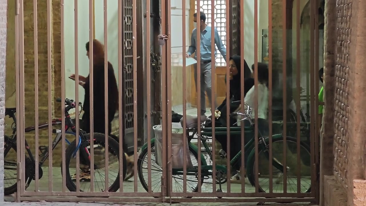 People Moving Through a Metal Gate in a Courtyard