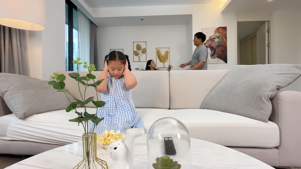 A child covers her ears during a parental argument in a bright, modern living room setting