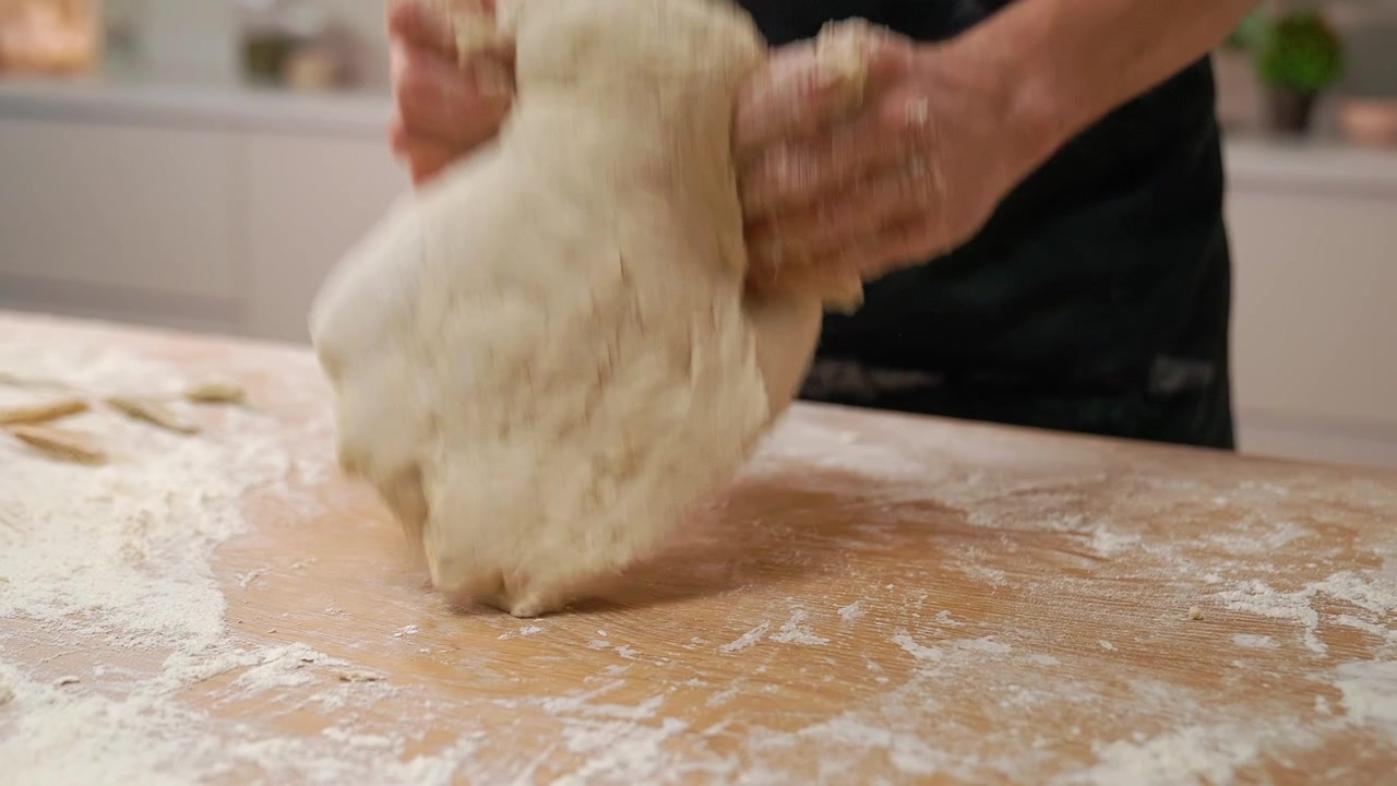 Primo piano di mani che impastano pasta fresca su un tavolo di legno infarinato