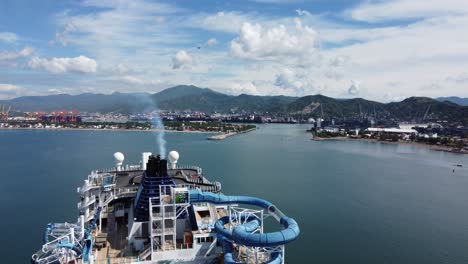 descenso aéreo lento revelando las cubiertas superiores de un crucero de lujo con toboganes de agua, piscinas y recreación al aire libre de varios niveles