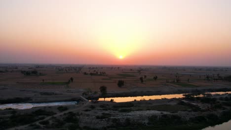 golden sun setting behind okara’s vast agricultural fields and reflective canal. punjab, pakistan