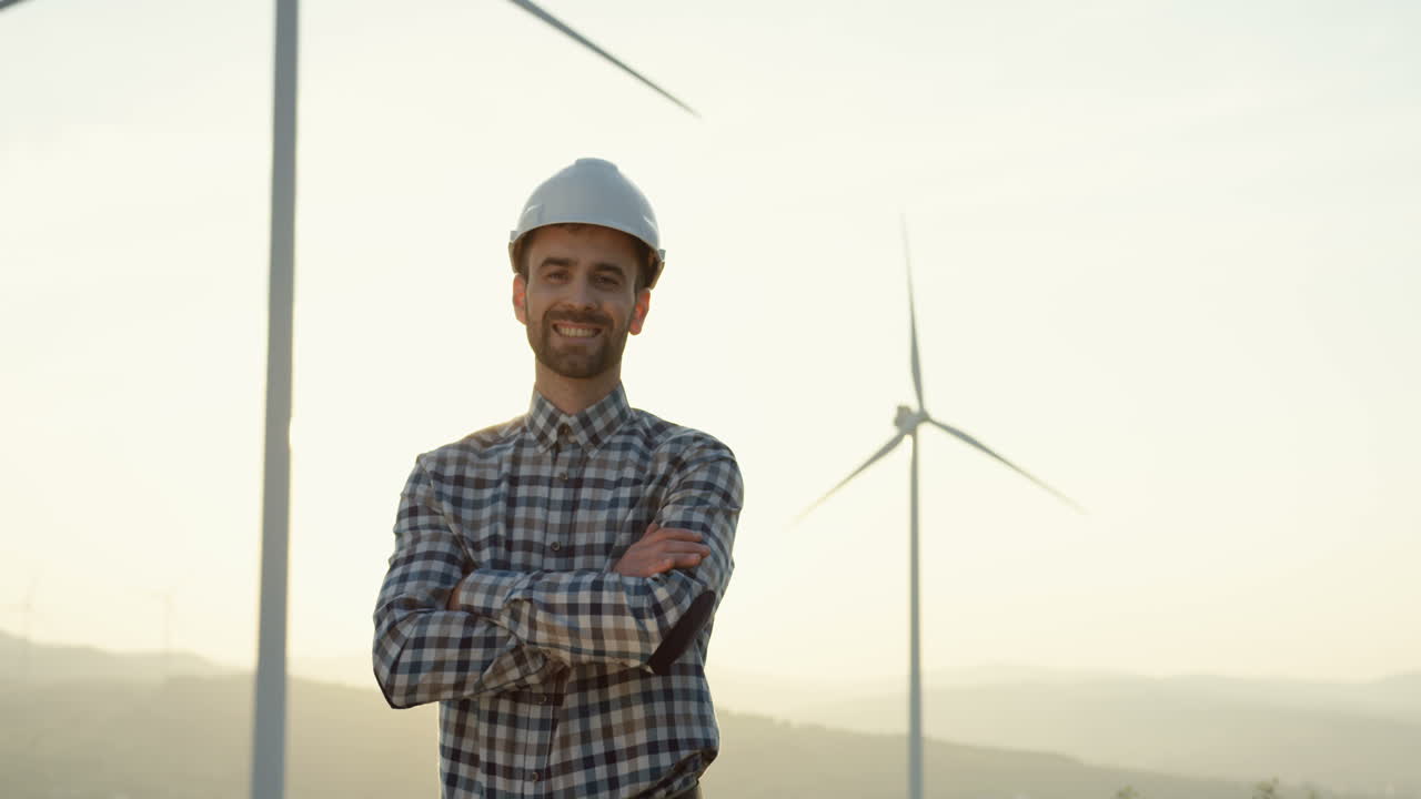 Caucasian engineer with helmet standing at the huge wind turbine station and looking at the horizon