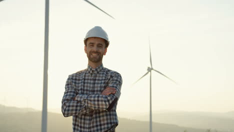 caucasian engineer with helmet standing at the huge wind turbine station and looking at the horizon