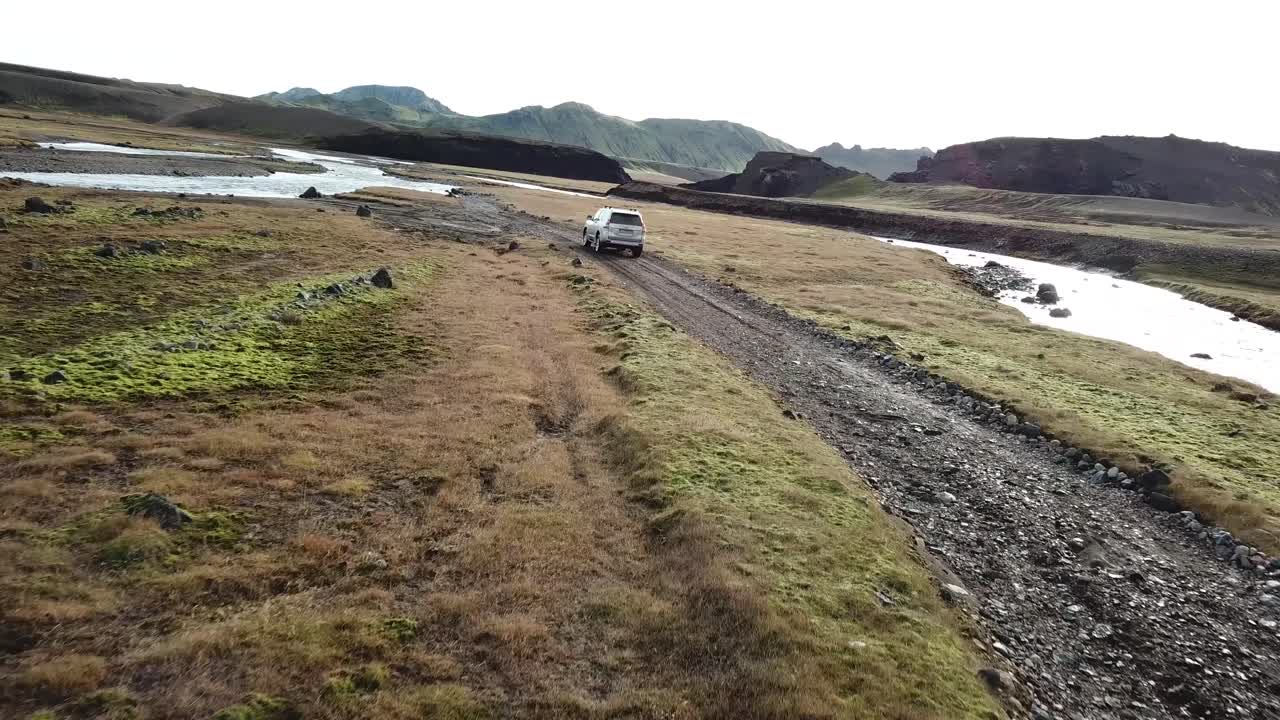 Four Wheel Vehicle in Humid Landscape of Iceland Highlands Moving in Valley Under Volcanic Mountains, Dramatic Tracking Aerial