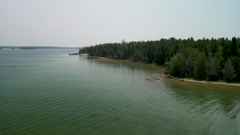 Aerial-view-down-coastline-of-forested-island,-Michigan