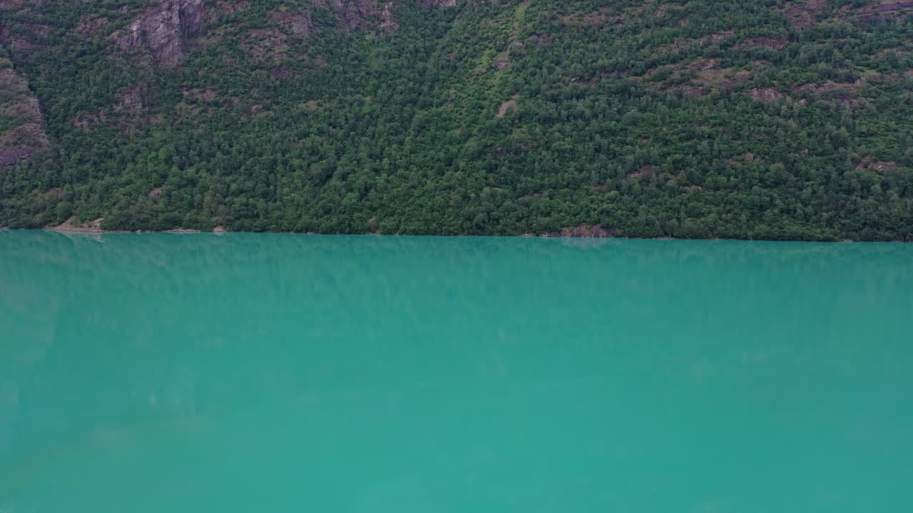 пресноводное озеро ольдеватн в норвежском согн-нордфьорде - медленная съемка с разрывом экрана между склоном горы и озером в центре - яркая зеленая ледниковая вода