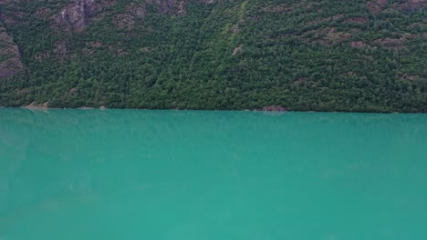 lago de agua dulce oldevatn en sogn nordfjord noruega - antena de movimiento lento hacia abajo con pantalla dividida entre la ladera de la montaña y el lago en el medio - agua glacial verde vibrante