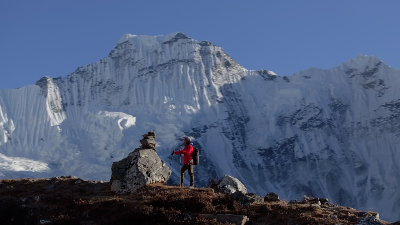 Ripresa con drone orbitante cattura un turista durante il trekking al Campo Base dell'Everest in Nepal, alla luce della sera, ammirando il panorama himalayano. La telecamera gira per mostrare le catene montuose con l'Ama Dablam sullo sfondo