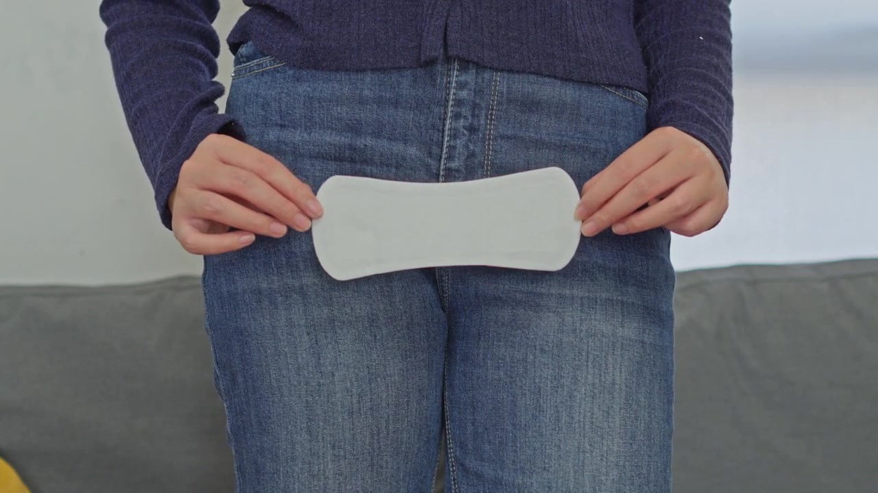 Close-up of woman in jeans holding an open sanitary liner in front of pelvis for feminine care