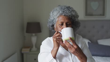 senior african american woman drinking coffee while sitting on the bed at home