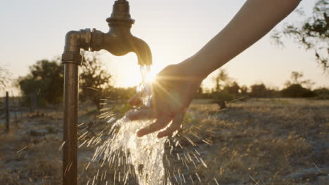 Frau-Wäscht-Sich-Bei-Sonnenuntergang-Auf-Einem-Ländlichen-Bauernhof-Die-Hand-Unter-Leitungswasser,-Das-Aus-Dem-Wasserhahn-Fließt