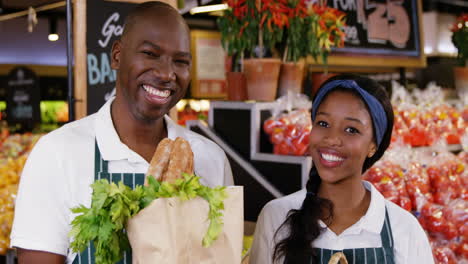 smiling staff holding basket and paper bag of vegetables