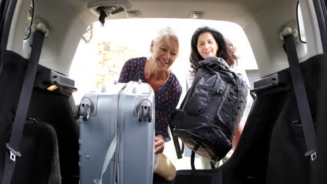 two happy diverse senior women putting suitcase and backpack into car on sunny day, slow motion