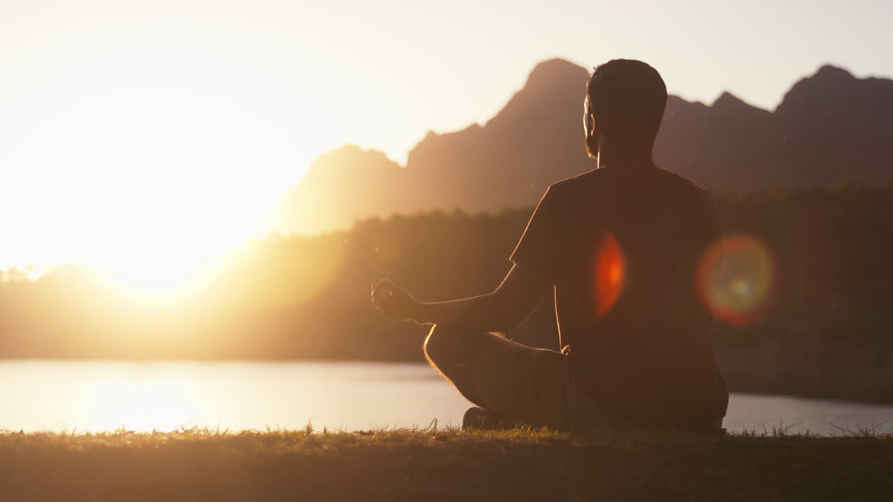 hombre meditando haciendo yoga junto a un hermoso lago y montañas al atardecer