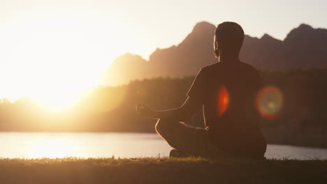 man meditating doing yoga by beautiful lake and mountains at sunset