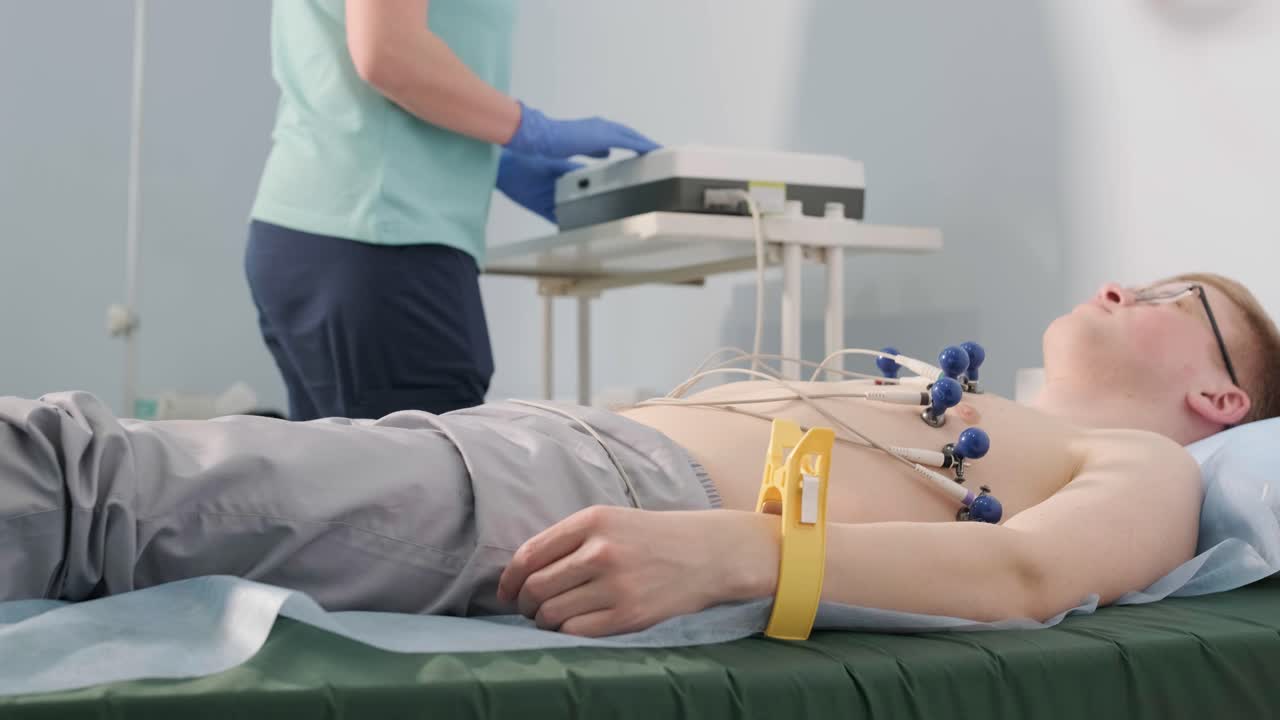 Exame cardíaco em um hospital com um cardiógrafo profissional. O paciente está deitado em uma cama com sensores conectados.