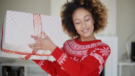 una chica hermosa sacudiendo su regalo de navidad en caja