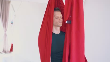 gentleman sits resting in special red hammock after workout