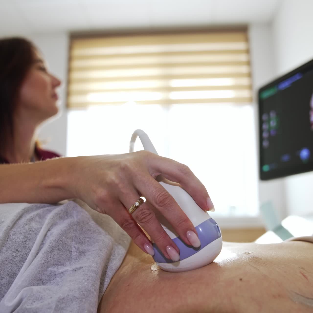 Pregnant lady lies her back to the doctor. Female physician moves the equipment transducer by the patient's abdomen side looking attentively on the screen