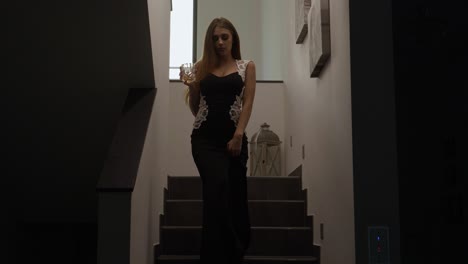 medium shot of a wealthy women walking down the stairs in a modern fashionable house with lights flicking in a dramatic manner