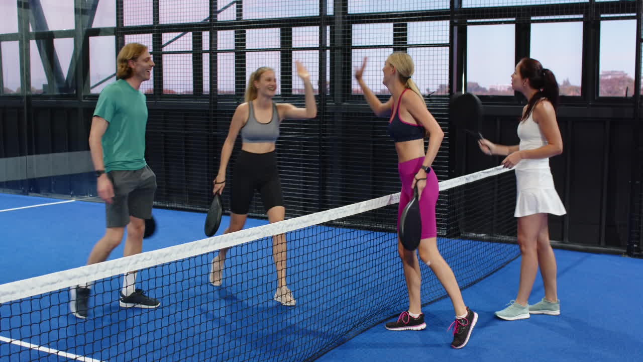 Group enjoying padel tennis match, smiling and holding rackets on indoor court