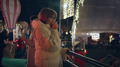 woman enjoying drink fairground at night with christmas lights. happy girl park