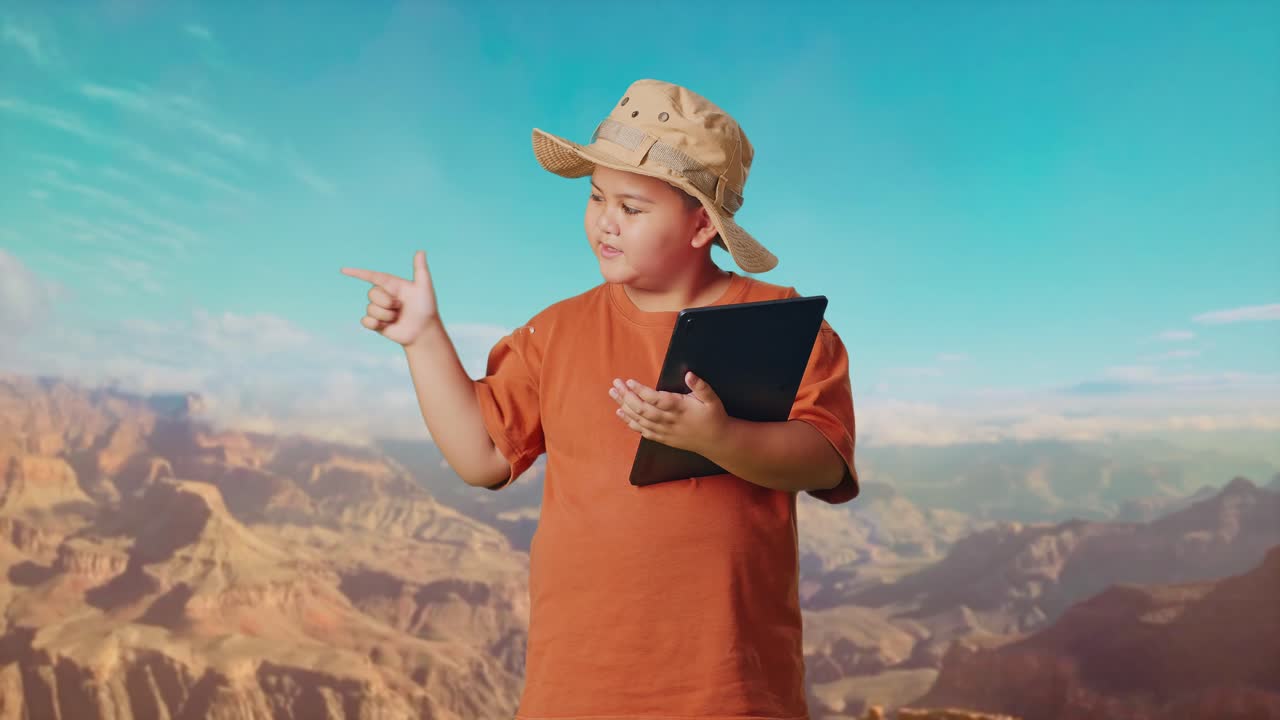 Asian Boy With A Hat Using A Tablet Then Smiling And Pointing To Side While Traveling At The Top Of Mountain. Boy Researcher Examines Something, Travel Tourism Adventure Concept
