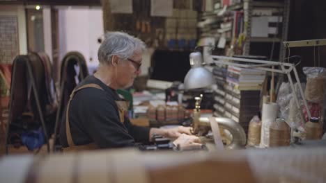 sideways shot of leather craftsman sitting while working in his laboratory