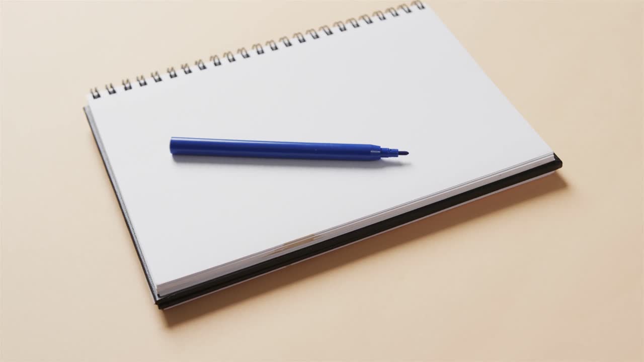 Close up of blue marker on notebook with beige background, in slow motion
