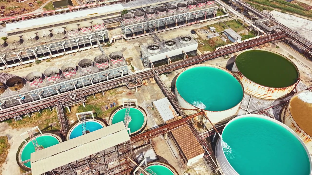 Bright colors in industrial tanks at a facility located near a city show different liquids in storage. The tanks are round with varied shades of blue and brown