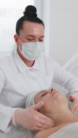 cosmetologist applying moisturizing medical chemical peeling cream mask on young adult woman face