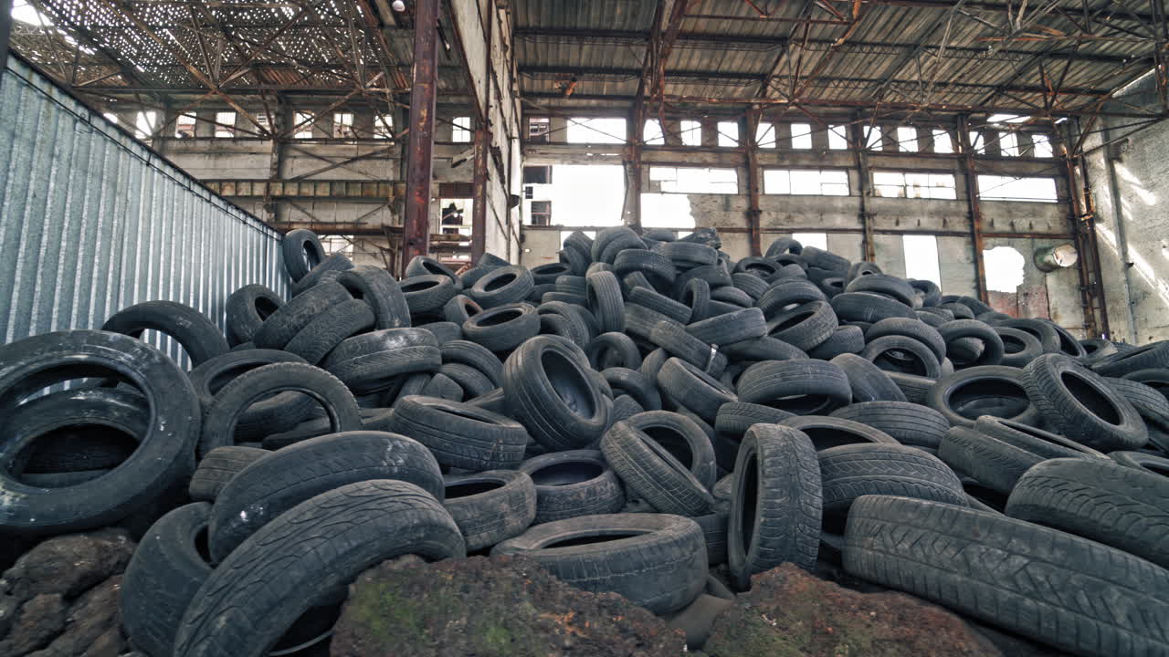 Black junk tires lying on the floor in the old abandoned building. Many used rubber tires from different vehicles are on a desolate plant inside.