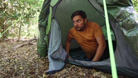 frightened man opens the zipper of the tent and looks around with a scared expression on his face