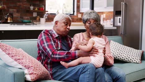 Grandparents-Sitting-On-Sofa-Playing-With-Baby-Granddaughter-At-Home