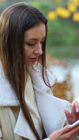 pretty lady with phone sitting in park. beautiful young outdoor communication. vertical video