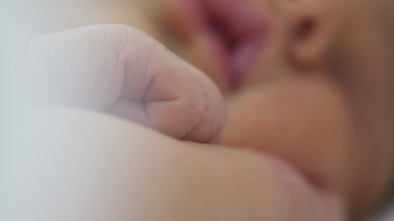 Neonato che muove lentamente le dita mentre dorme, primo piano