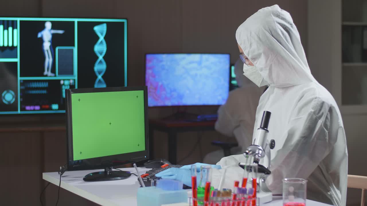 Asian Doctor In Protective Suit Working With Mock Up Green Screen Computer Display In A Modern Lab. Laboratory Assistant Workplace