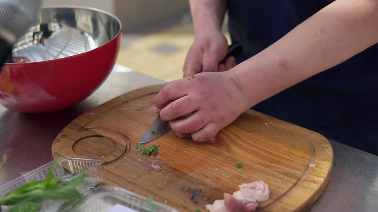 Person's hands cutting a piece of raw meat using a butcher's knife on a wooden surface outside. Barbeque preparation. shot in 4k