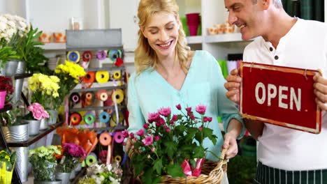 smiling florist holding open sign on slate in flower shop