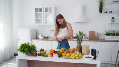 Attractive girl with meter in the kitchen. Fresh organic food on the table. Young woman is measuring her waist at home. Concept of losing weight.