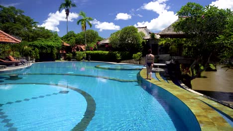 woman walking along luxury pool at a bali  hotel resort  wearing a two piece bikini on a nice sunny day. great travel vacation destination.