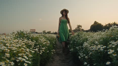 woman in a green dress walking through a field of flowers at sunset