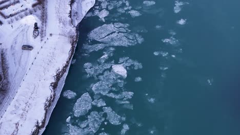 aerial top down of flowing ice floe on selfoss river in iceland. snowy winter day with parking car. global warming and melting concept theme.